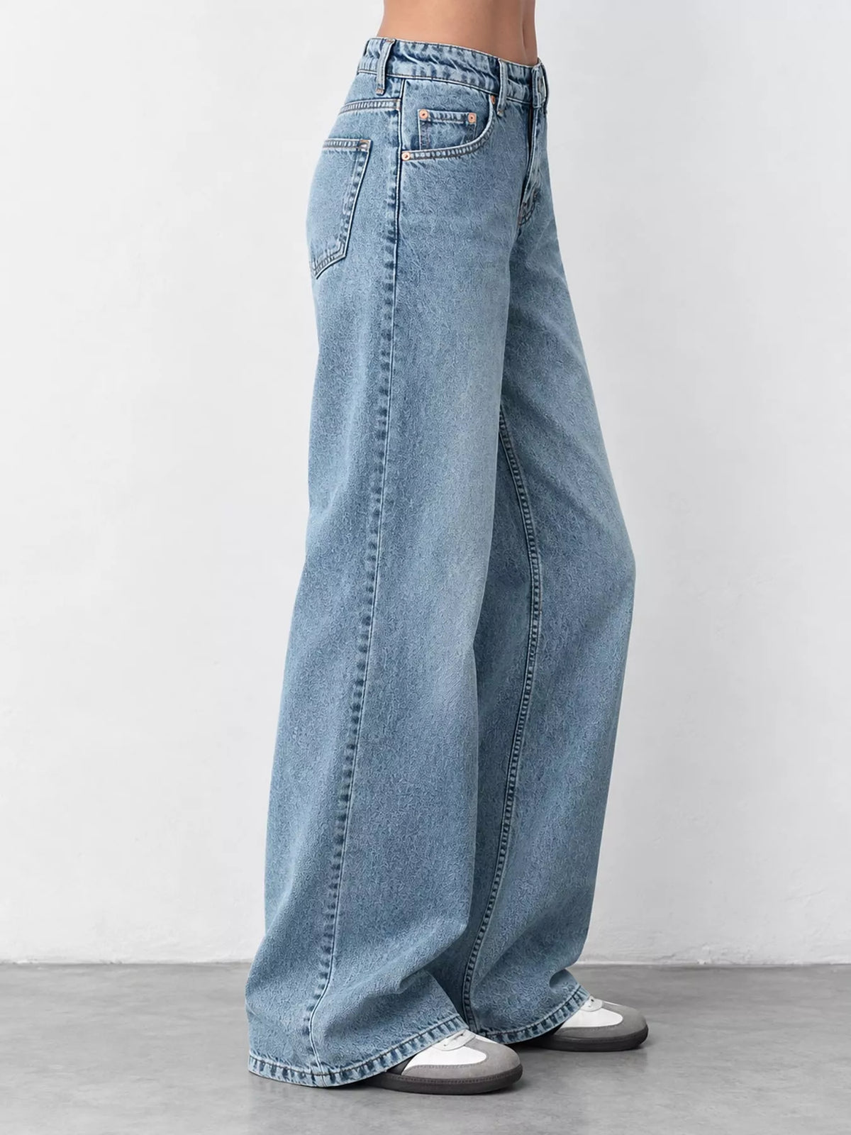Light blue wide-leg denim jeans shown on a model from the waist down, paired with white sneakers, against a neutral studio background.