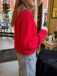 Person wearing a red sweater holding a coffee cup in an urban setting.
