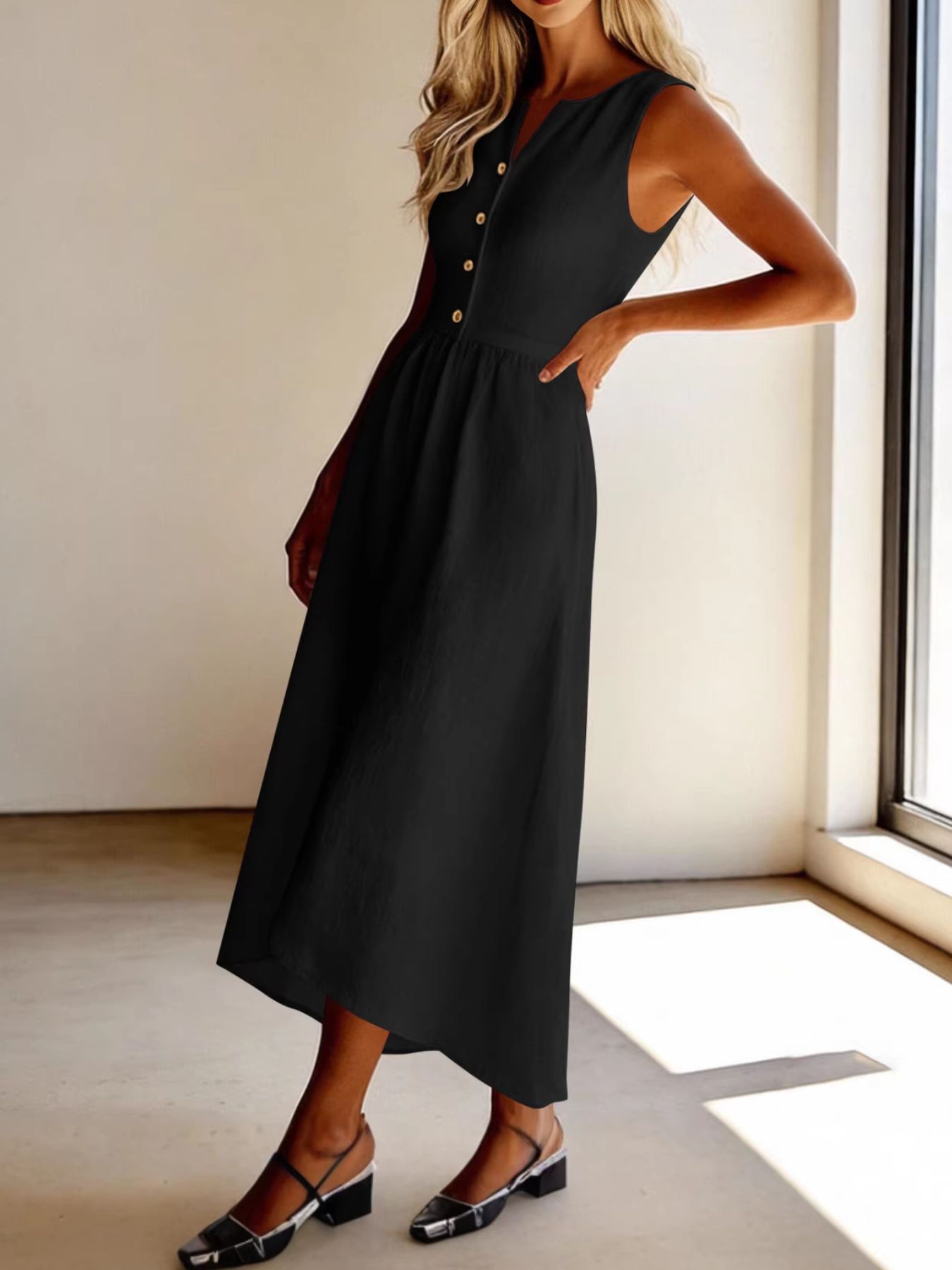 Woman wearing a black sleeveless dress standing indoors near a window.