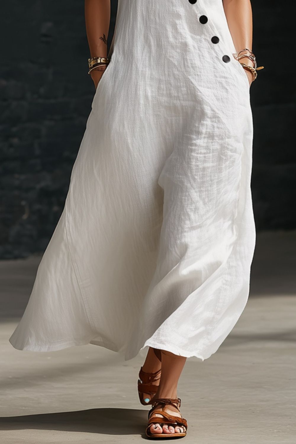 Person wearing a white dress with black buttons and brown sandals on a neutral background