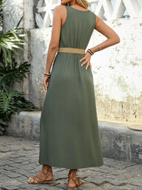 Woman wearing a green dress with a belt, standing on a stone path with plants in the background.
