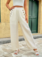 Person wearing white pants with button details in an outdoor setting.