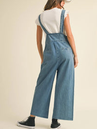 Person wearing blue denim overalls on a plain background