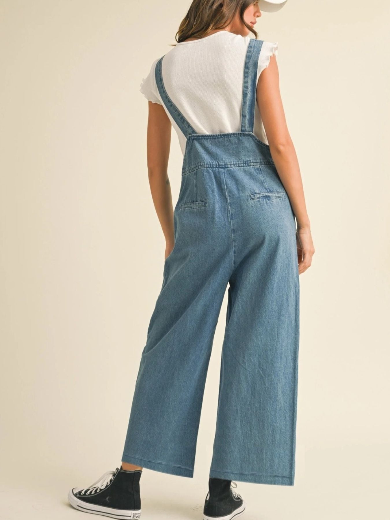 Person wearing blue denim overalls on a plain background