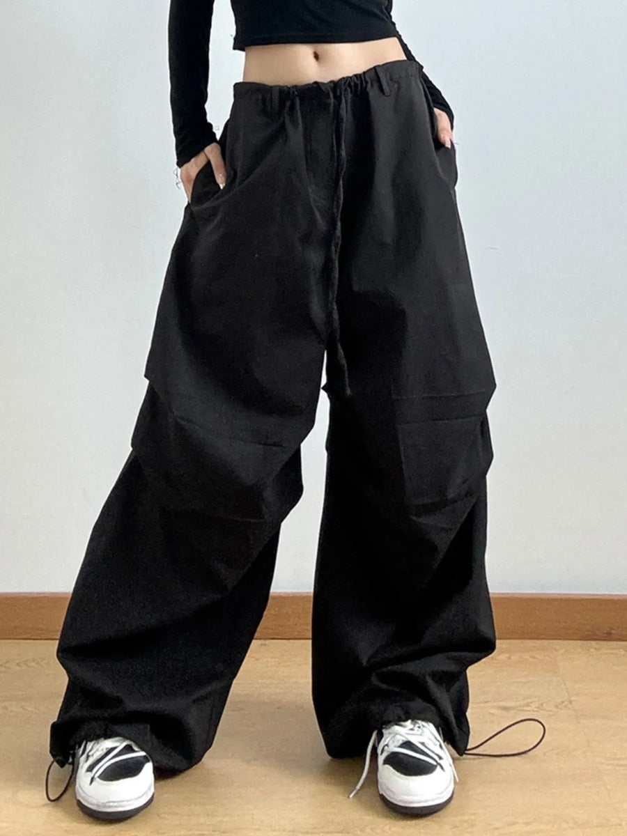 Person wearing black wide-leg pants and black shoes on a light gray background