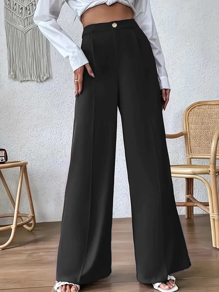 Person wearing black wide-leg pants and a white top in a room with a textured wall and wooden floor.