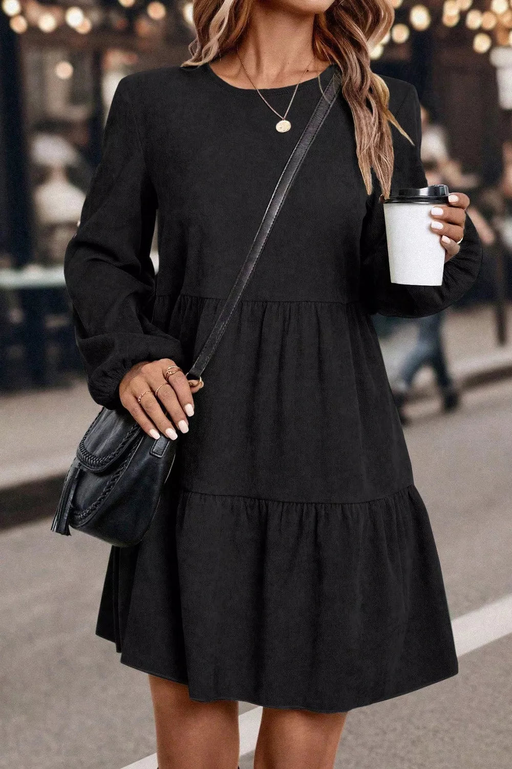Woman wearing a black dress holding a coffee cup on a street.