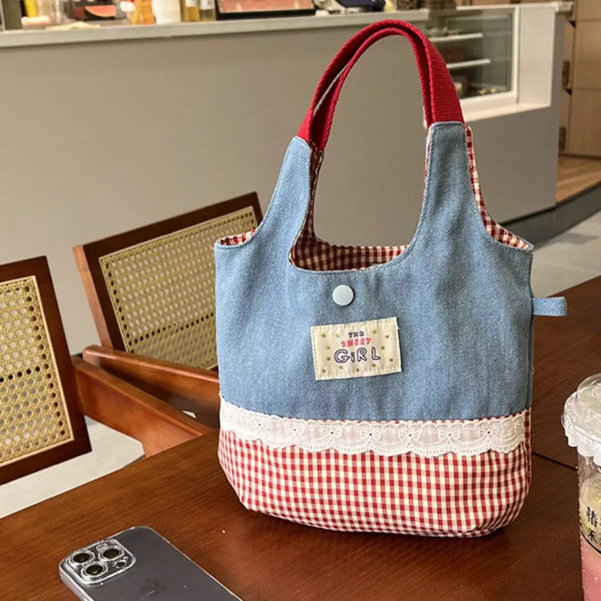 Blue and red checkered tote bag with a 'Girl' patch on a wooden table.
