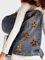 Person wearing a denim jacket with floral embellishments on a white background