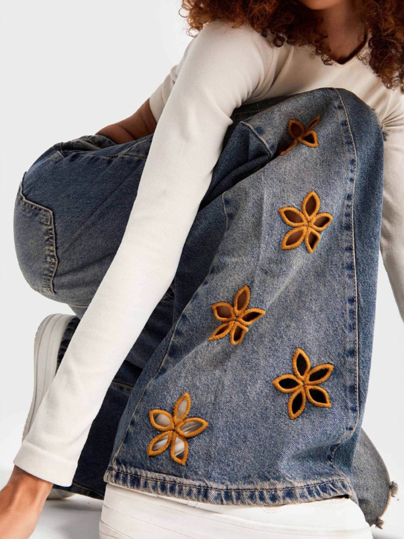 Person wearing a denim jacket with floral embellishments on a white background