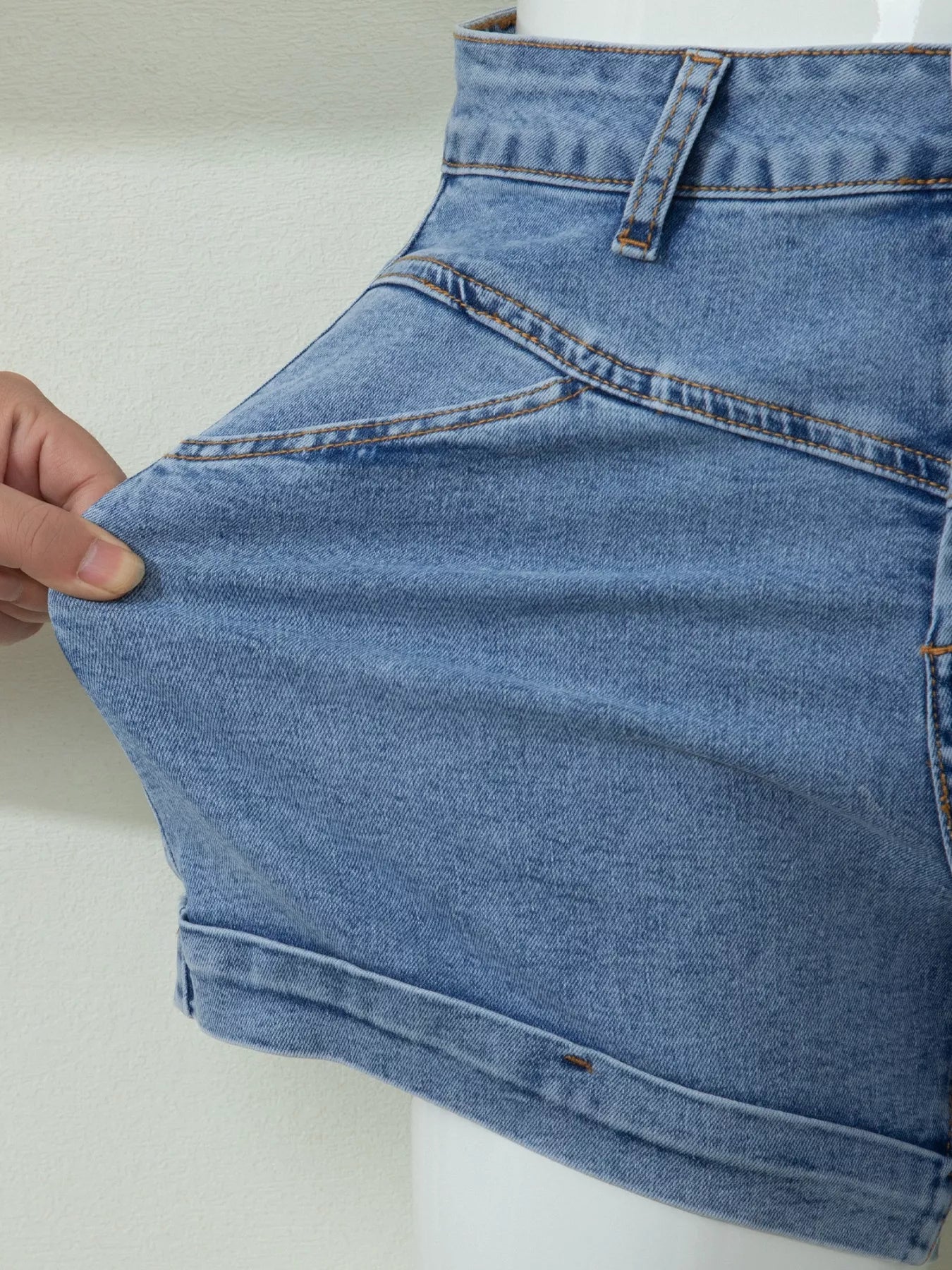 Close-up of blue denim shorts held by a hand on a white background