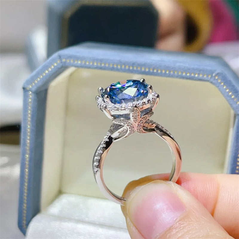 Silver ring with a blue gemstone held by a hand, displayed in a blue jewelry box.