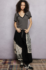 Woman wearing a gray top and black patterned pants against a plain background