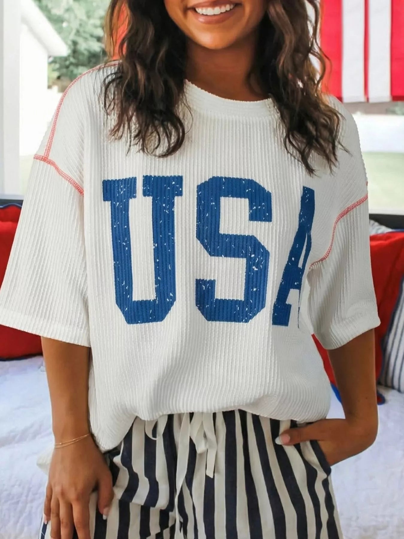 Person wearing a white t-shirt with 'USA' printed in blue, standing outdoors.