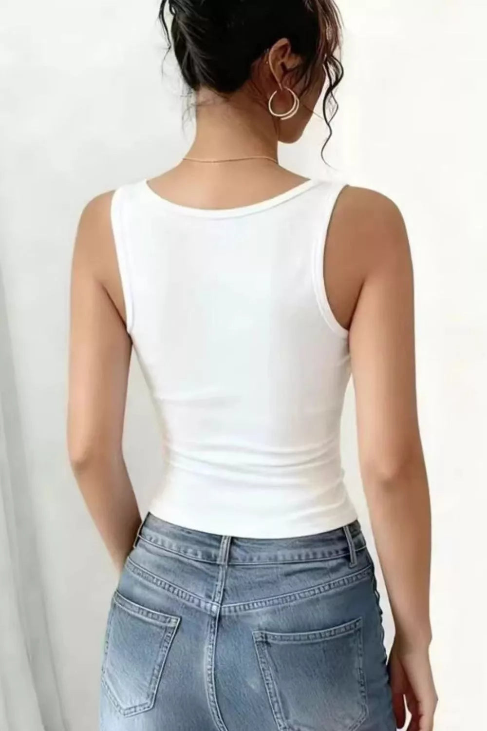 Person wearing a white tank top and blue jeans on a plain background