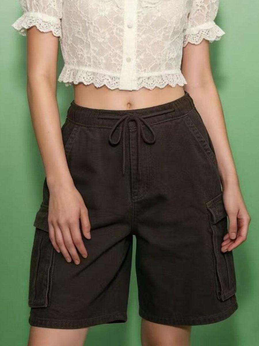 Person wearing a white lace top and brown cargo shorts against a green background