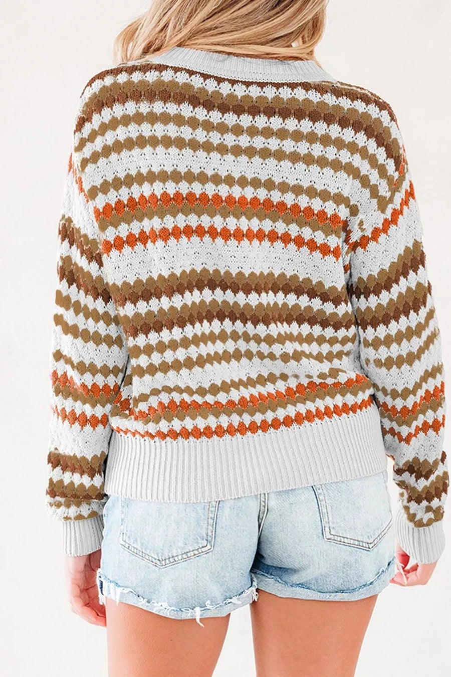 A woman shown from the back wearing a knit cardigan with horizontal wavy stripes in brown, rust orange, and white, paired with light-wash denim shorts.