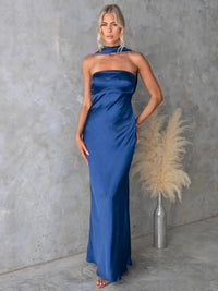 Woman in a blue strapless gown standing against a gray wall with a decorative plant.