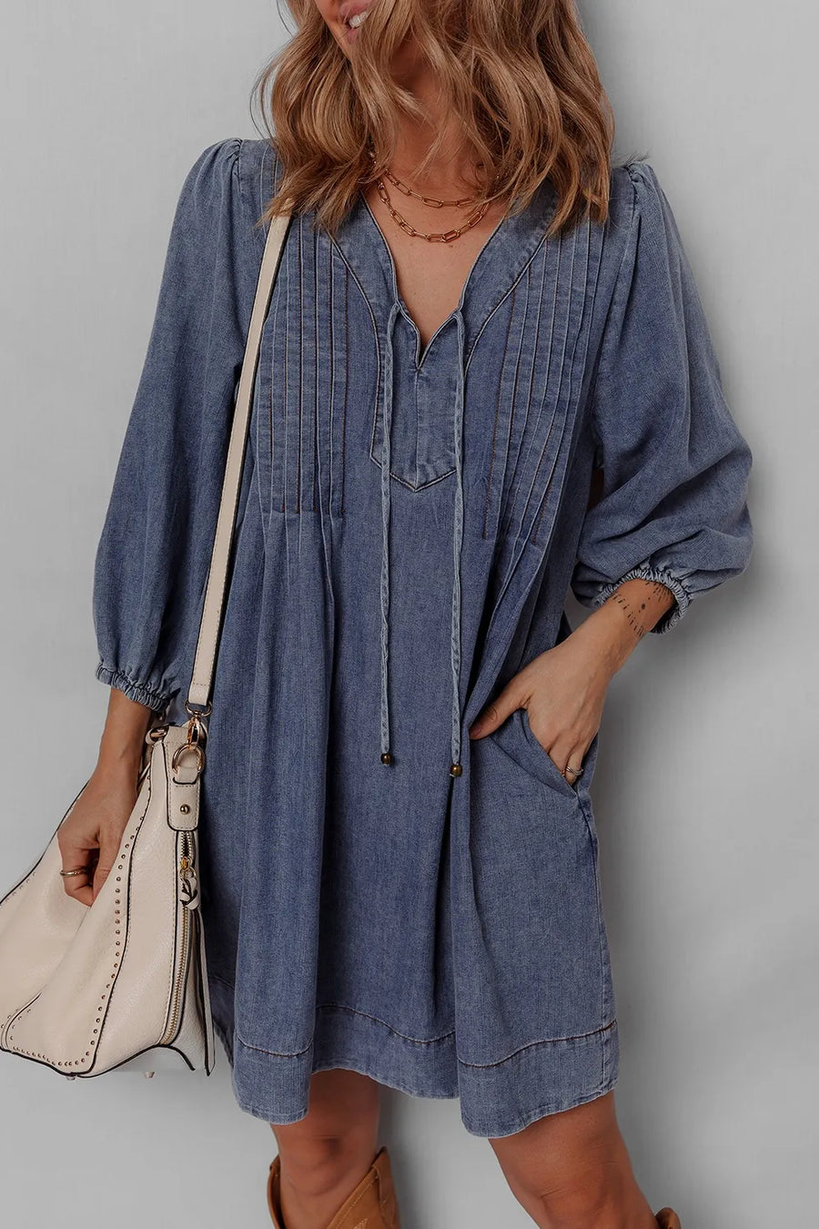 Woman wearing a blue dress with long sleeves against a gray background