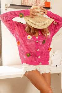 Person wearing a pink crochet cardigan with floral decorations, sitting on a white surface.