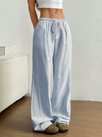 Person wearing light blue and white striped wide-leg pants in a minimal indoor setting.