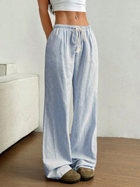 Person wearing light blue and white striped wide-leg pants in a minimal indoor setting.