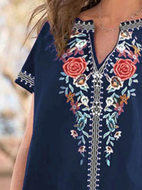 Navy blue dress with floral embroidery on a blurred natural background