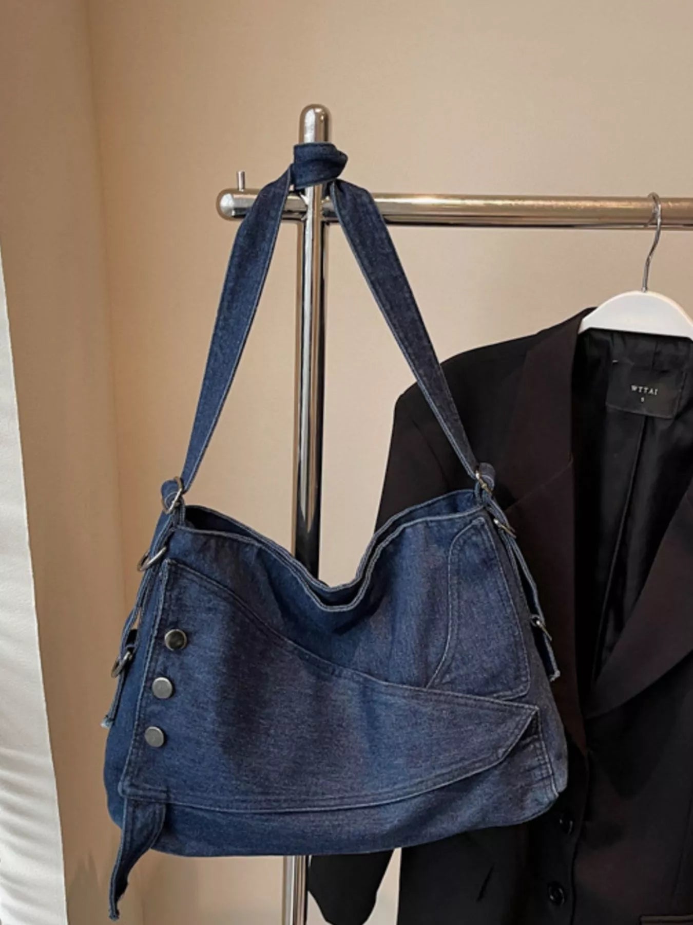 Blue denim handbag hanging on a rack with a coat in the background
