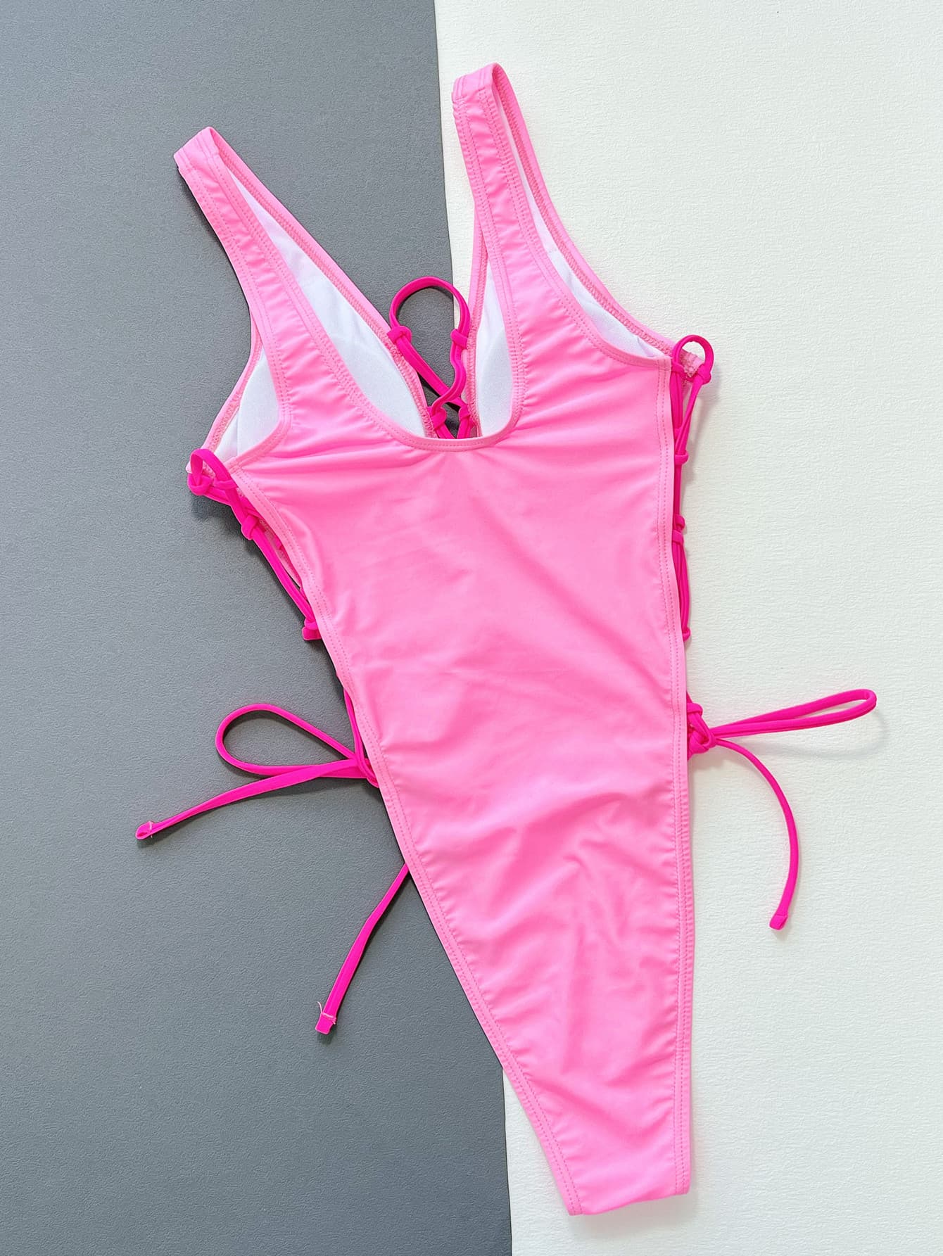 Pink swimsuit with tie details on a gray and white background