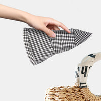 Hand holding a black and white checkered fabric item with a woven basket and newspaper in the background.