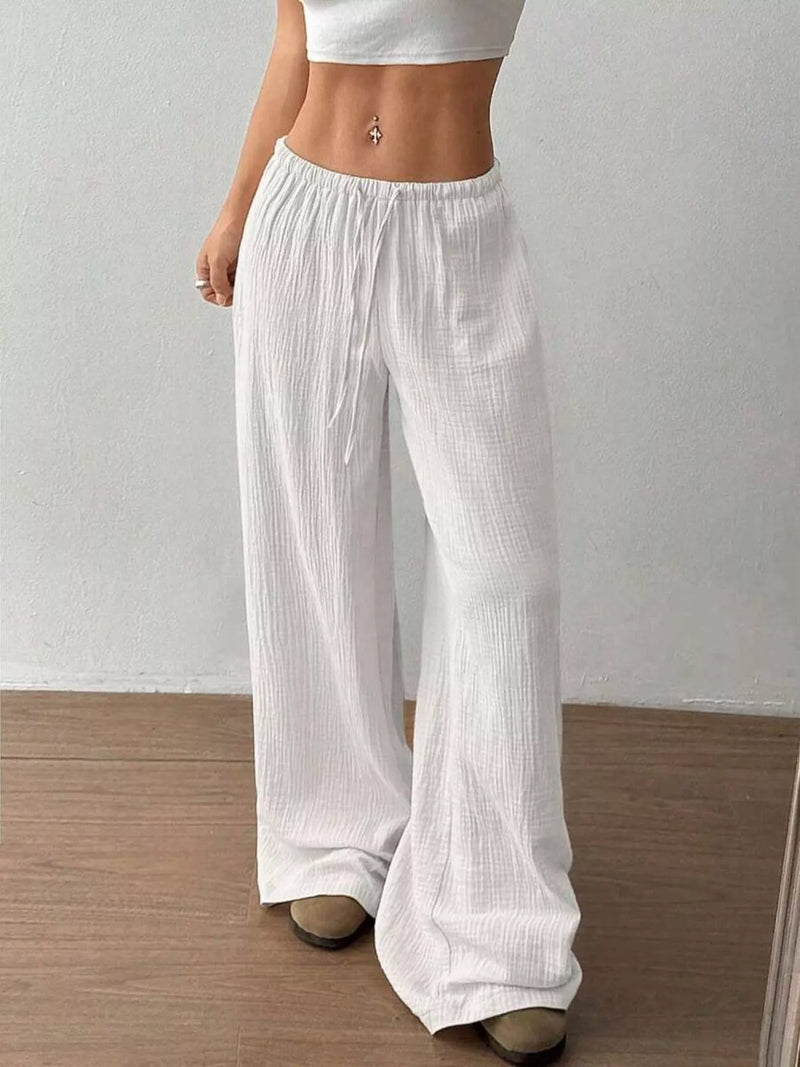 Person wearing white wide-leg pants and a white top against a plain background