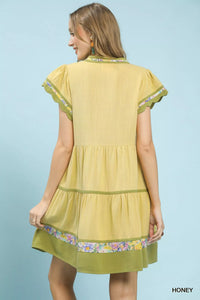 Woman wearing a yellow dress with floral trim on a light blue background