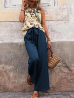 Woman wearing a floral top and blue pants with a straw bag against a textured wall.