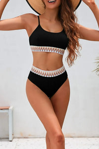 Woman wearing a black bikini with a white and orange patterned waistband against a light background.