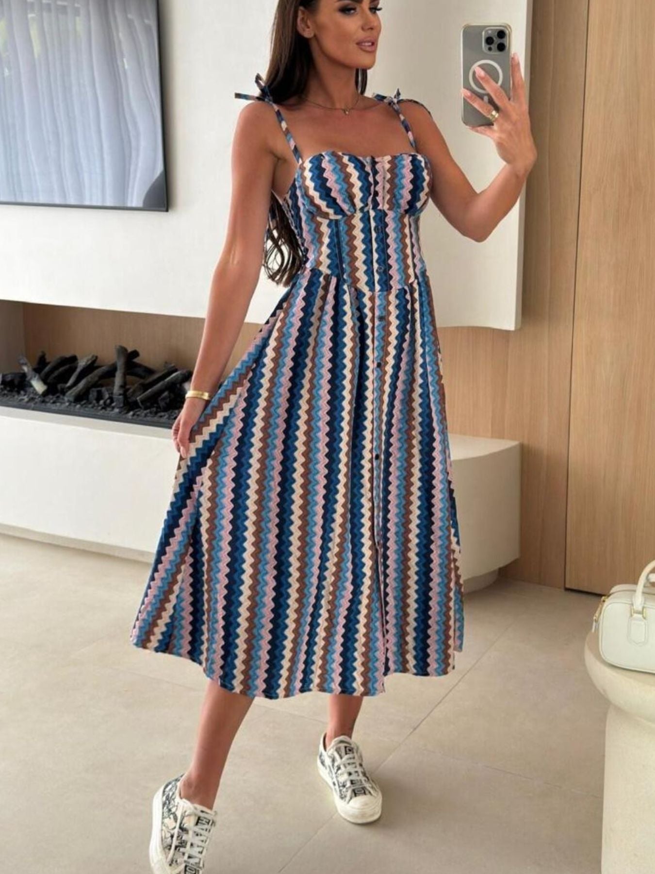 Woman taking a mirror selfie wearing a striped dress in a modern room.