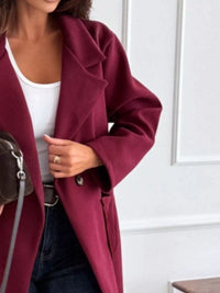 Person wearing a burgundy coat over a white top and dark jeans, holding a brown bag.