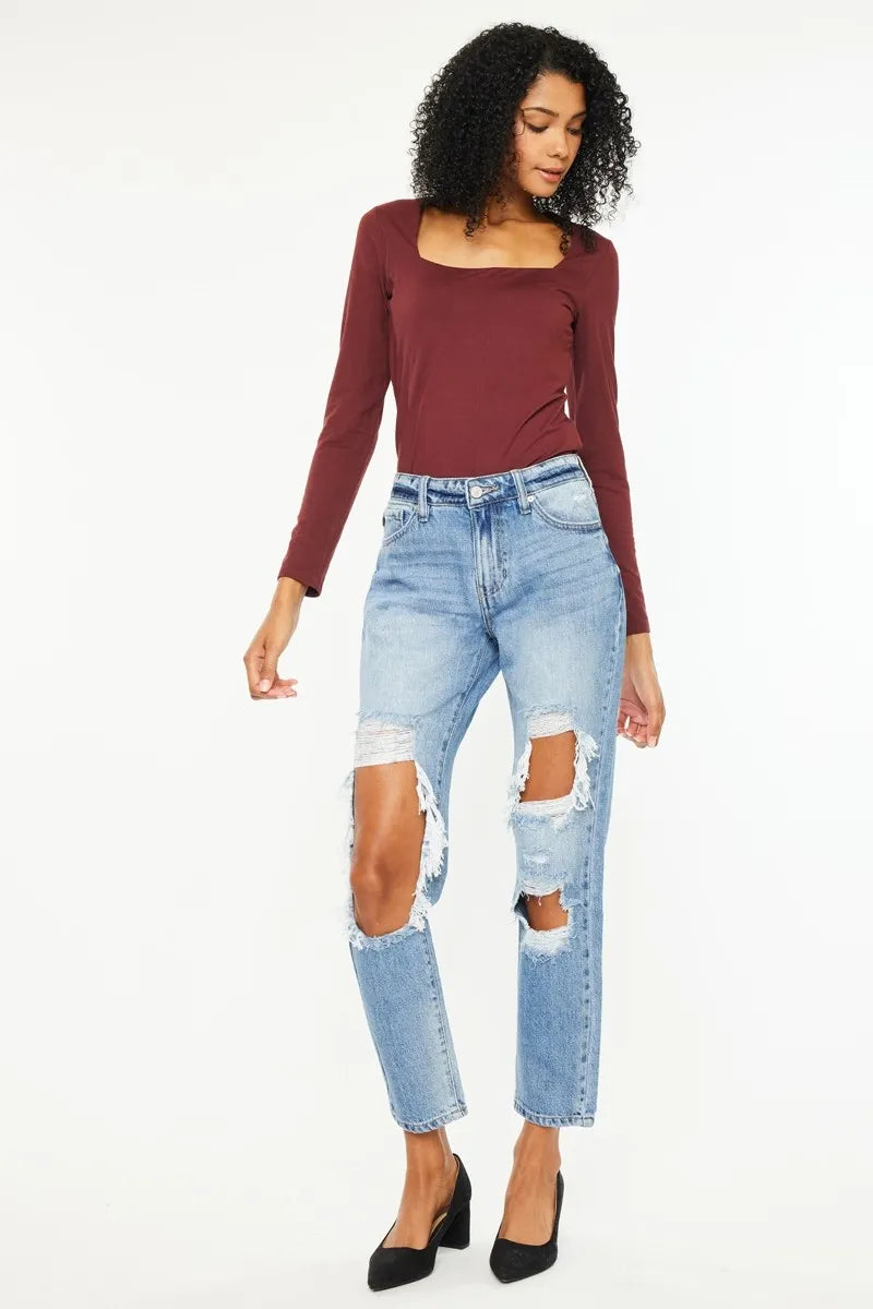 Woman wearing a burgundy long-sleeve top and distressed blue jeans on a white background