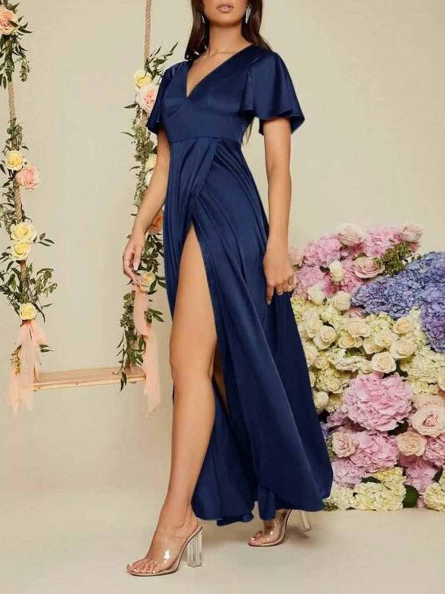 Woman wearing a navy blue dress with a high slit in front of floral decorations.