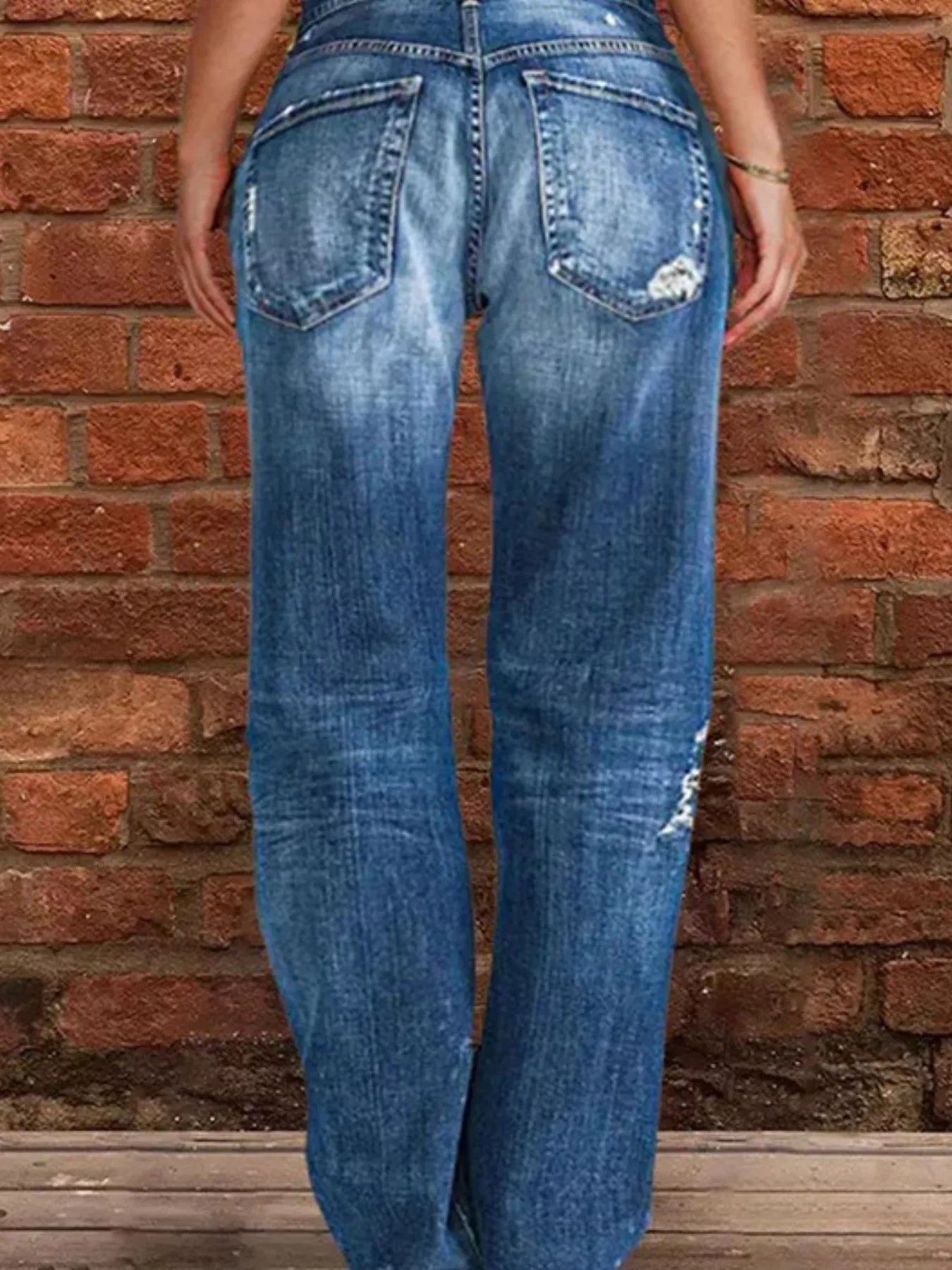 Blue jeans worn by a person against a brick wall.