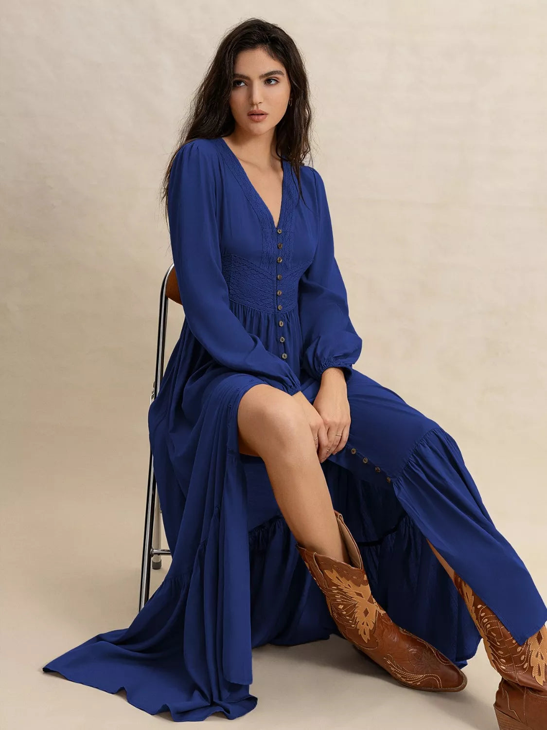 Woman in a blue dress and brown boots sitting on a chair against a beige background
