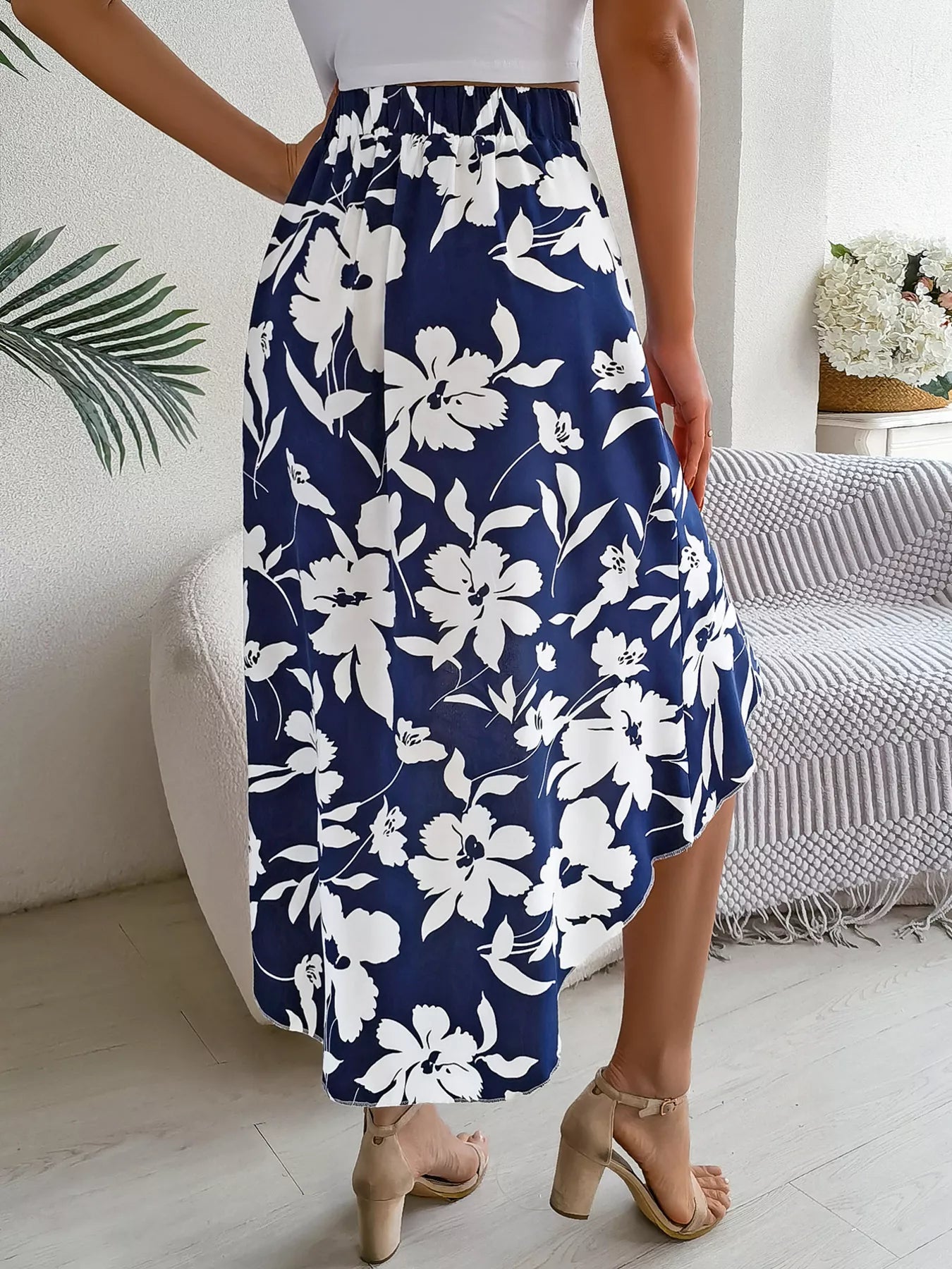 Person wearing a navy blue floral skirt in a room with a bed and plant.