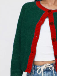 Green cardigan with red trim over a white shirt and blue jeans on a light gray background