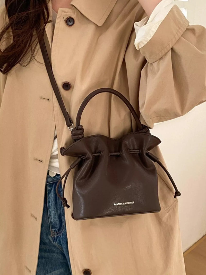 Person wearing a beige trench coat with a brown leather drawstring bag.
