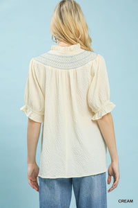 Woman wearing a cream-colored blouse with lace details on a light blue background