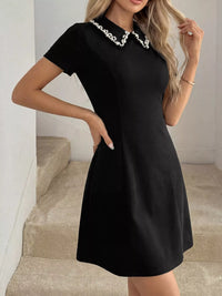 Woman wearing a black dress with a pearl collar in an indoor setting.