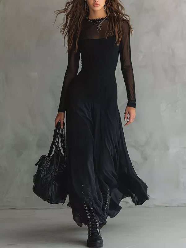 A woman models a long black dress with sheer long sleeves, a square neckline, and a flowing skirt, styled with black lace-up boots and a large black handbag against a textured gray studio backdrop.