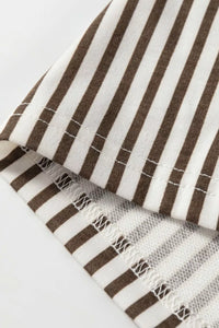 Close-up of a brown and white striped fabric with tassels on a light gray background