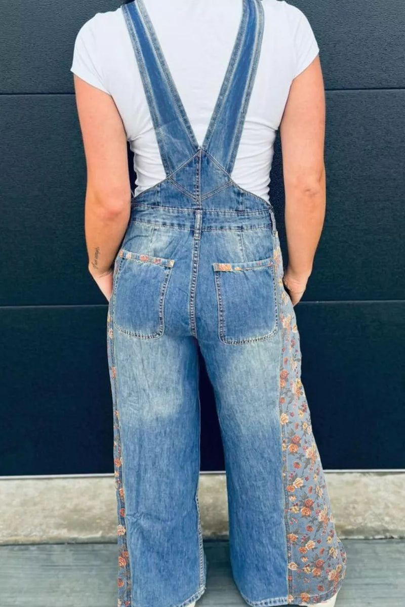 Person wearing floral-patterned denim overalls against a blue wall.