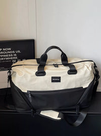 Beige and black duffel bag on a dark surface with a white wall background