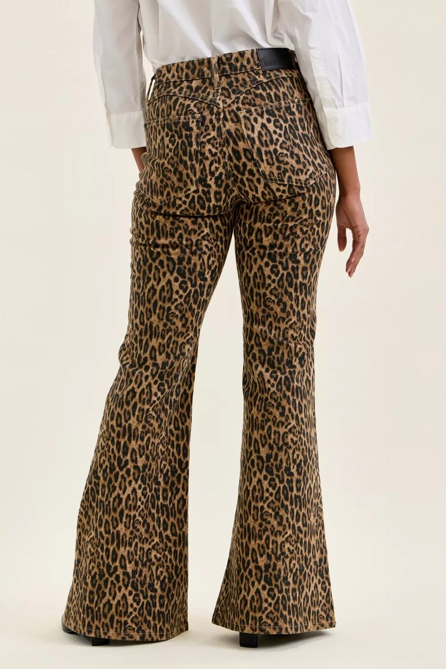 Leopard print flared pants worn with a white shirt on a beige background